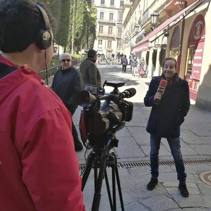 Grabación de una entrevista callejera en el centro de una ciudad, con camarógrafo de ISOPRO operando una cámara profesional y reportero sosteniendo un micrófono rojo mientras transeúntes pasan por detrás.