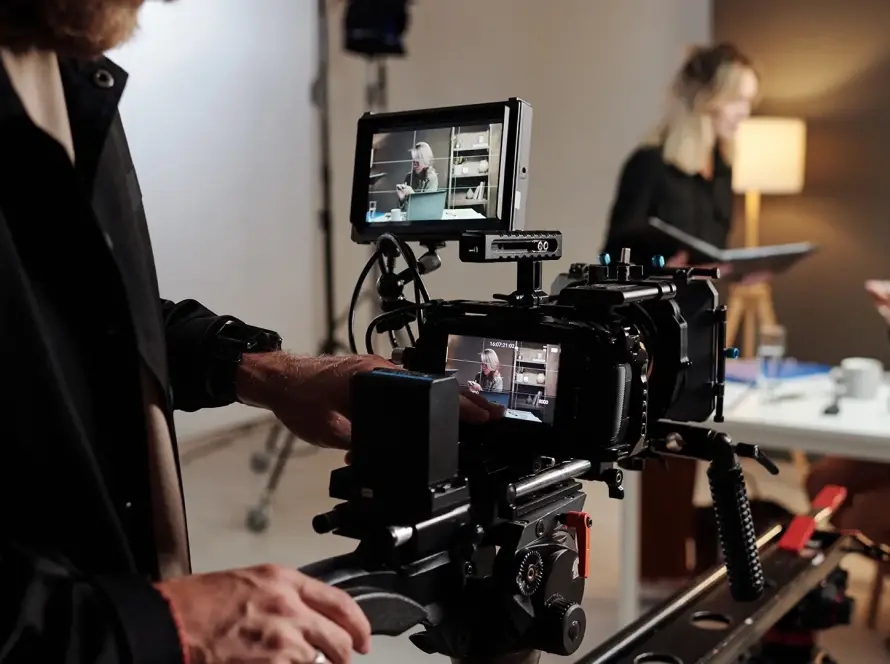 Rodaje en estudio con cámara de cine profesional sobre rieles enfocando a dos mujeres en segundo plano, una con portátil y otra con libreta, en un entorno corporativo moderno y bien iluminado.