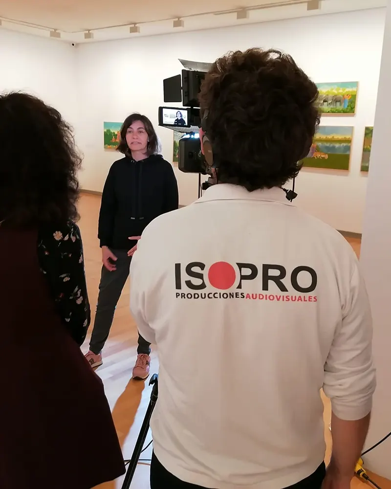 Grabación de una entrevista en una galería de arte, con técnica de cámara a cargo del equipo de ISOPRO Producciones Audiovisuales, identificado con camiseta corporativa.