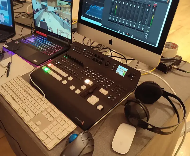 Mesa de realización con monitores, mezcladora de vídeo Blackmagic, ordenador iMac y portátil durante la retransmisión en directo de un evento con múltiples cámaras.